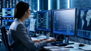 Cybersecurity analyst coding at multi-monitor workstation